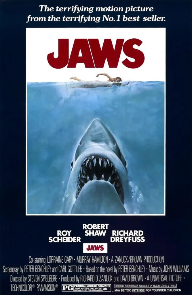 Jaws movie poster featuring the iconic image of a massive great white shark rising from the depths with its jaws wide open, heading toward an unsuspecting female swimmer at the surface. The bold red title ‘JAWS’ looms above, capturing the film’s suspense and terror.