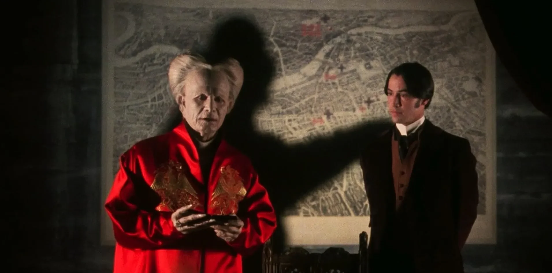 Gary Oldman as Count Dracula in his red robe, casting a monstrous shadow behind him while speaking with Jonathan Harker in Bram Stoker’s Dracula (1992).