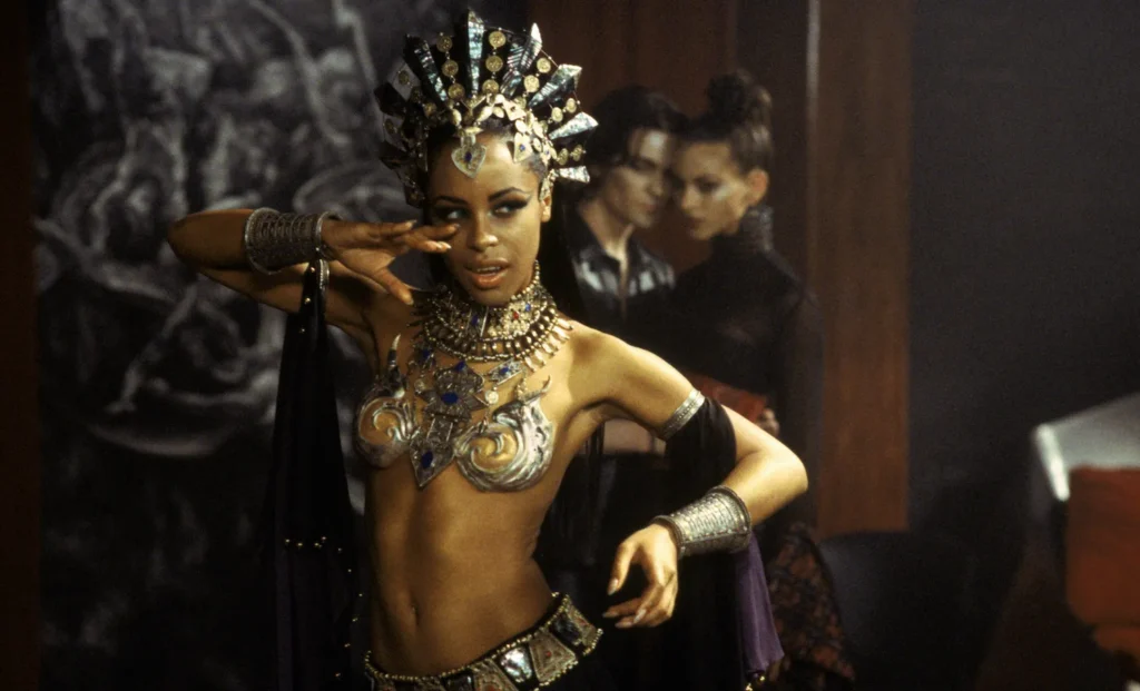 Aaliyah as Queen Akasha in Queen of the Damned (2002), wearing ornate jewelry and a jeweled crown while striking a commanding pose.